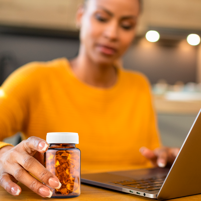 Woman holding supplement bottle sitting at a computer